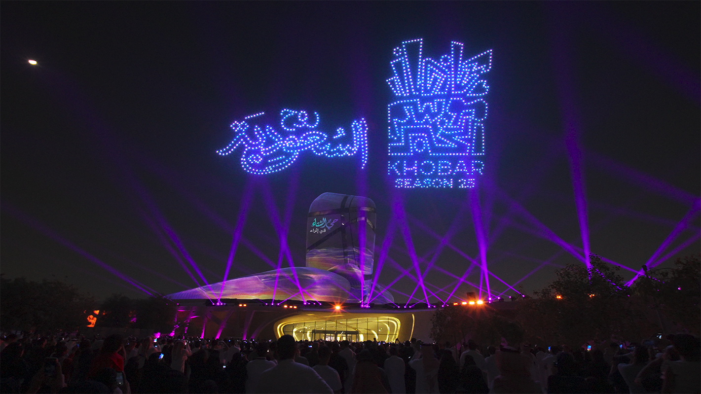 A crowd of spectators watches a night drone show at the Ithra Cultural Center. In the sky, drones form the inscriptions 