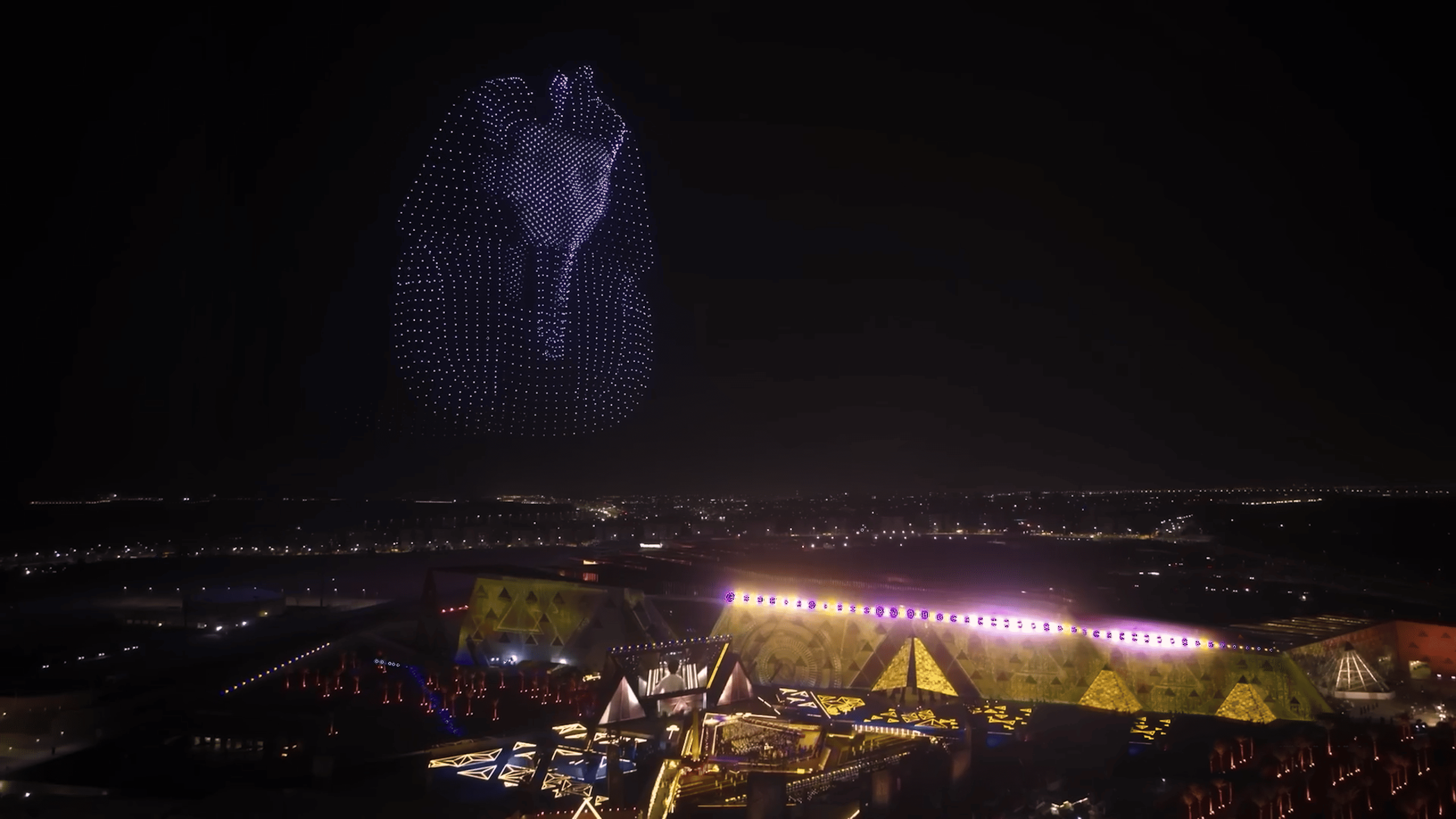 During the Lumasky drone show at the opening of the museum in Egypt, drones form a glowing pharaoh figure in the night sky above the illuminated buildings of the complex.
