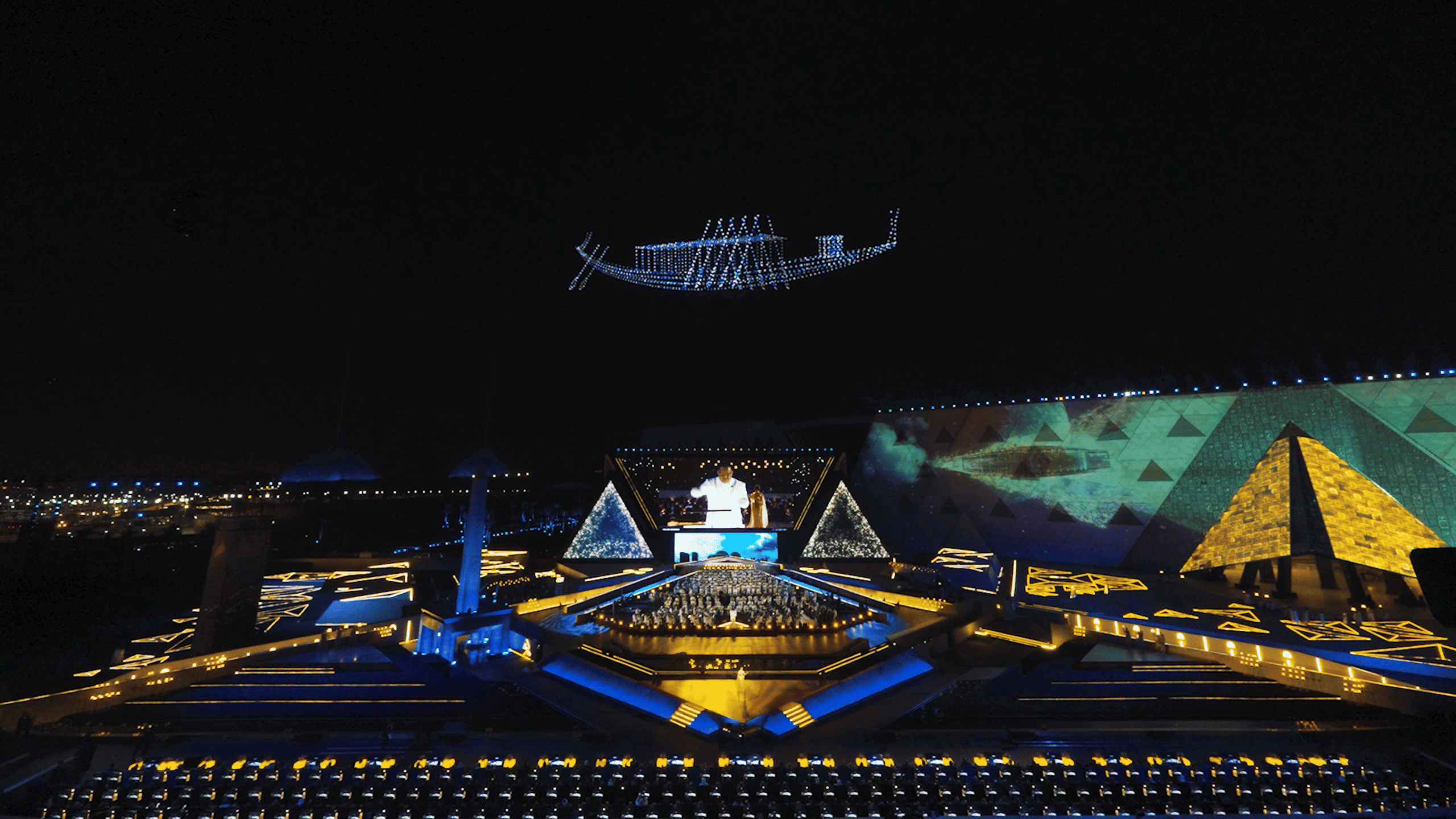 During the Lumasky drone show at the opening of the museum in Egypt, drones line up in the sky in the shape of an ancient Egyptian boat hovering over the illuminated stage and pyramids.
