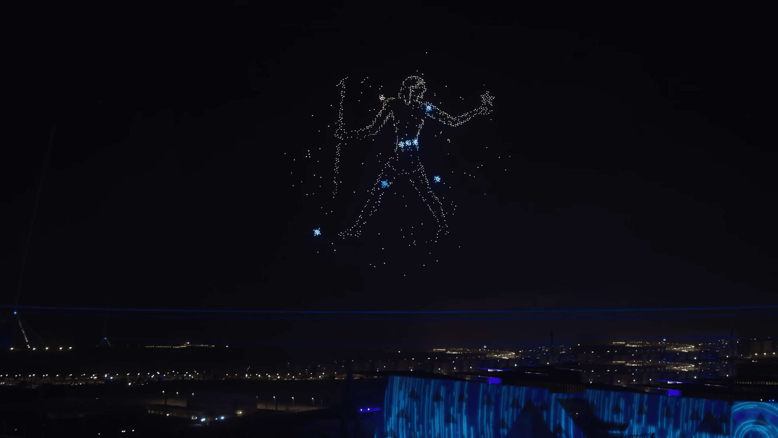 During the Lumasky drone show at the opening of the museum in Egypt, drones form a figure in the night sky resembling a hunter from a constellation, with glowing stars around. The illuminated buildings of the museum complex are visible below.