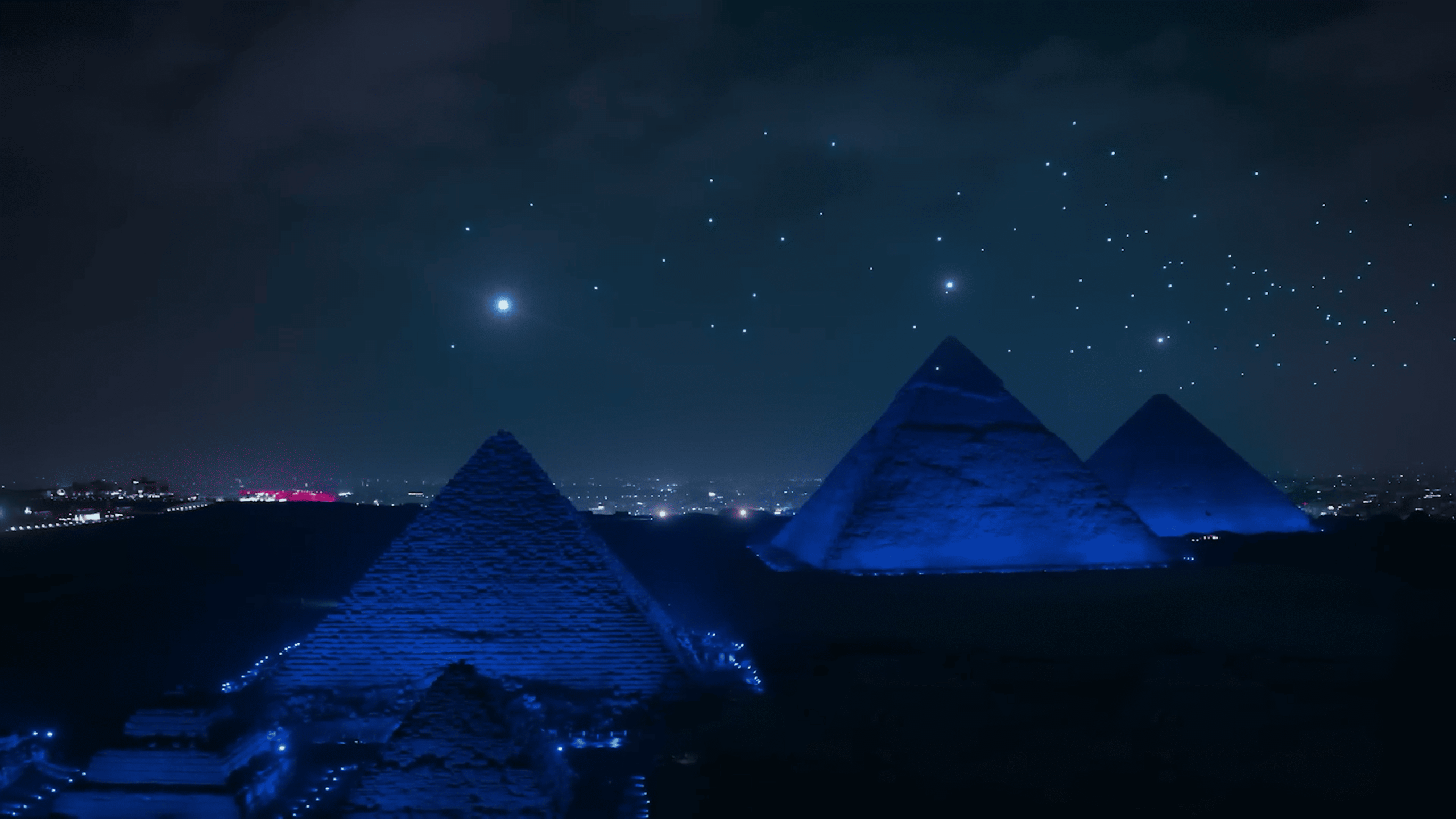 During the Lumasky drone show at the opening of the museum in Egypt, drones create a pattern of luminous dots in the night sky above the pyramids, illuminated by deep blue light.