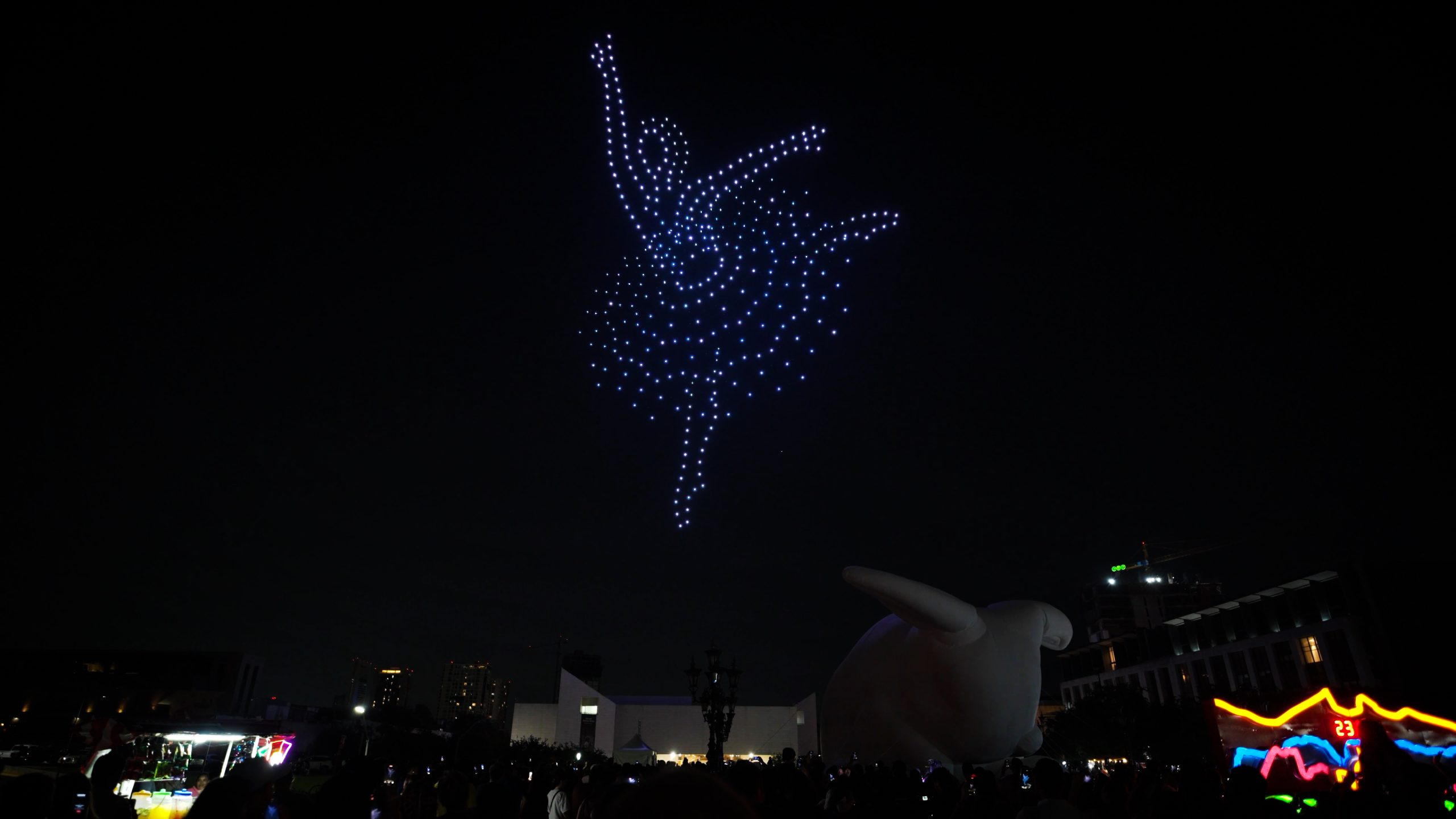 During the 500 Drone Light Show at Santa Lucía Festival in Monterrey, drones form a dancer's figure in a dynamic pose in the night sky, created by a multitude of blue luminous dots.