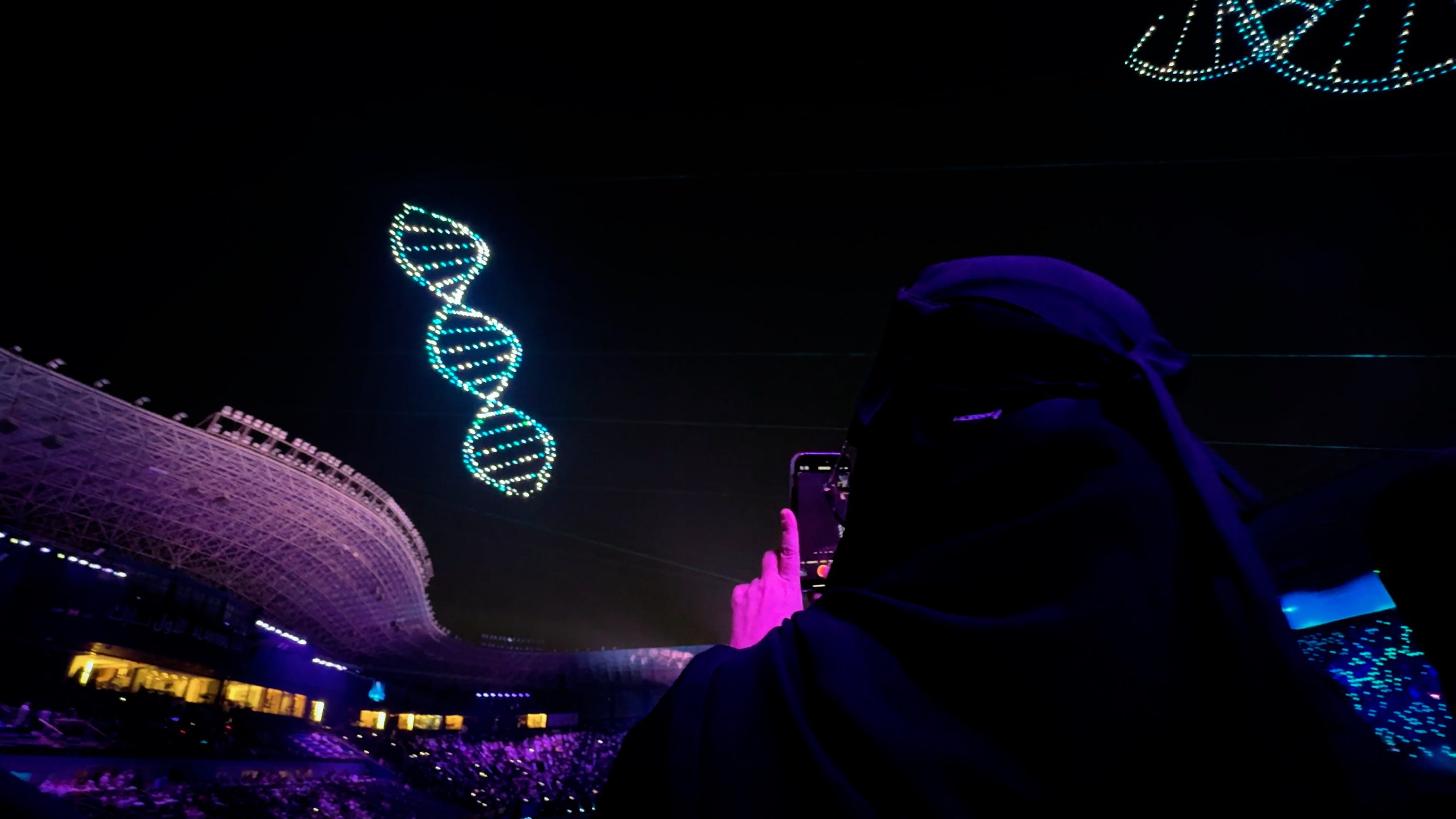 During the Lumasky Drone Show, drones form a glowing DNA spiral in the night sky at the “Riyadh's Doctors Got a 2,900 Drone Show for Graduation” event, watched by the audience at the stadium.
