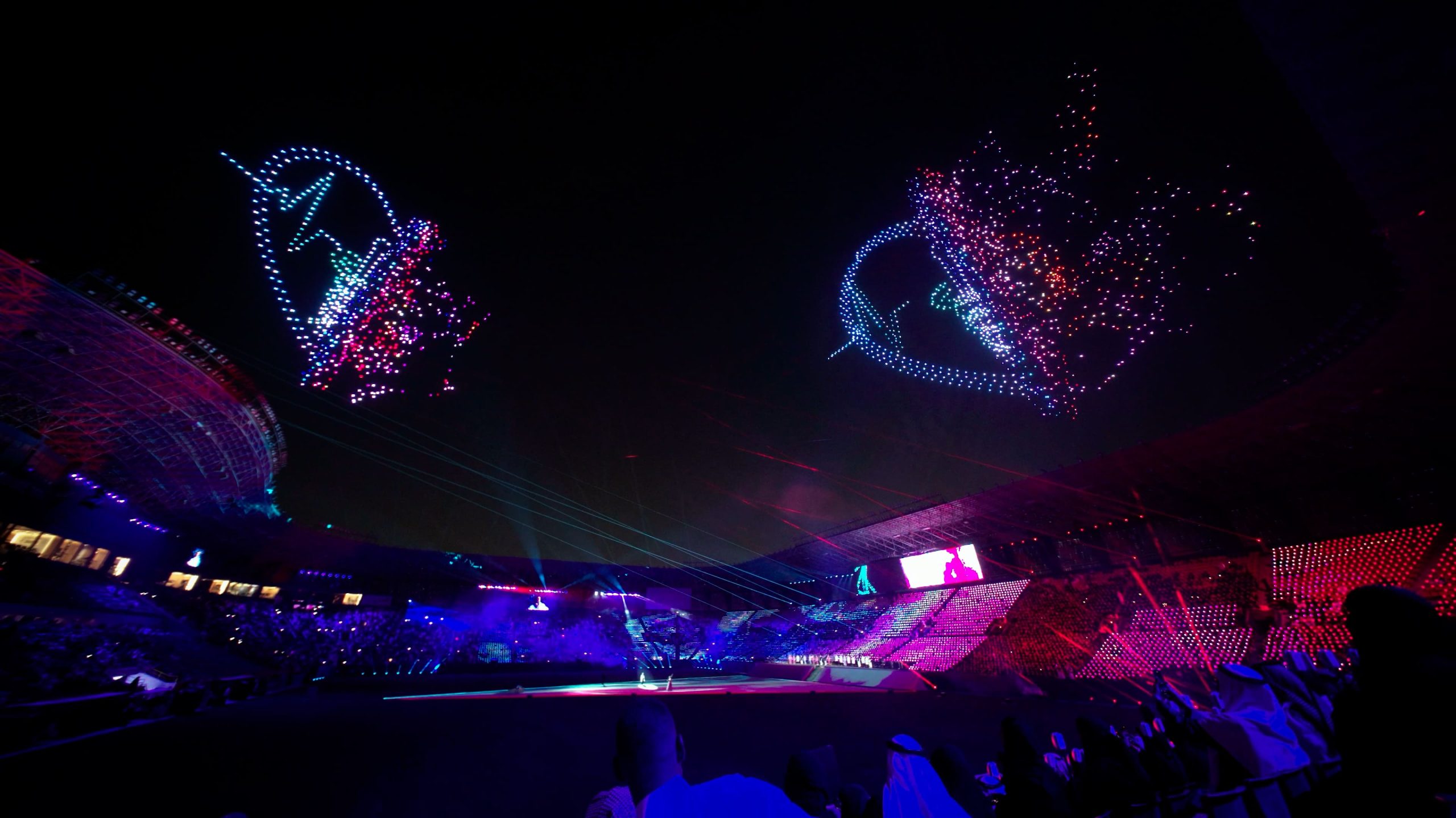 During the Lumasky Drone Show, drones form medical symbols and abstract light shapes in the night sky at the “Riyadh's Doctors Got a 2,900 Drone Show for Graduation” event, above a lighted stadium.