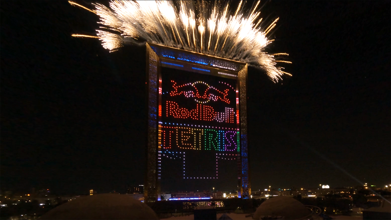 During the Lumasky Drone Show at the Red Bull Tetris Final in Dubai, the building is illuminated with Tetris light graphics, and pyrotechnic effects flash above the roof.