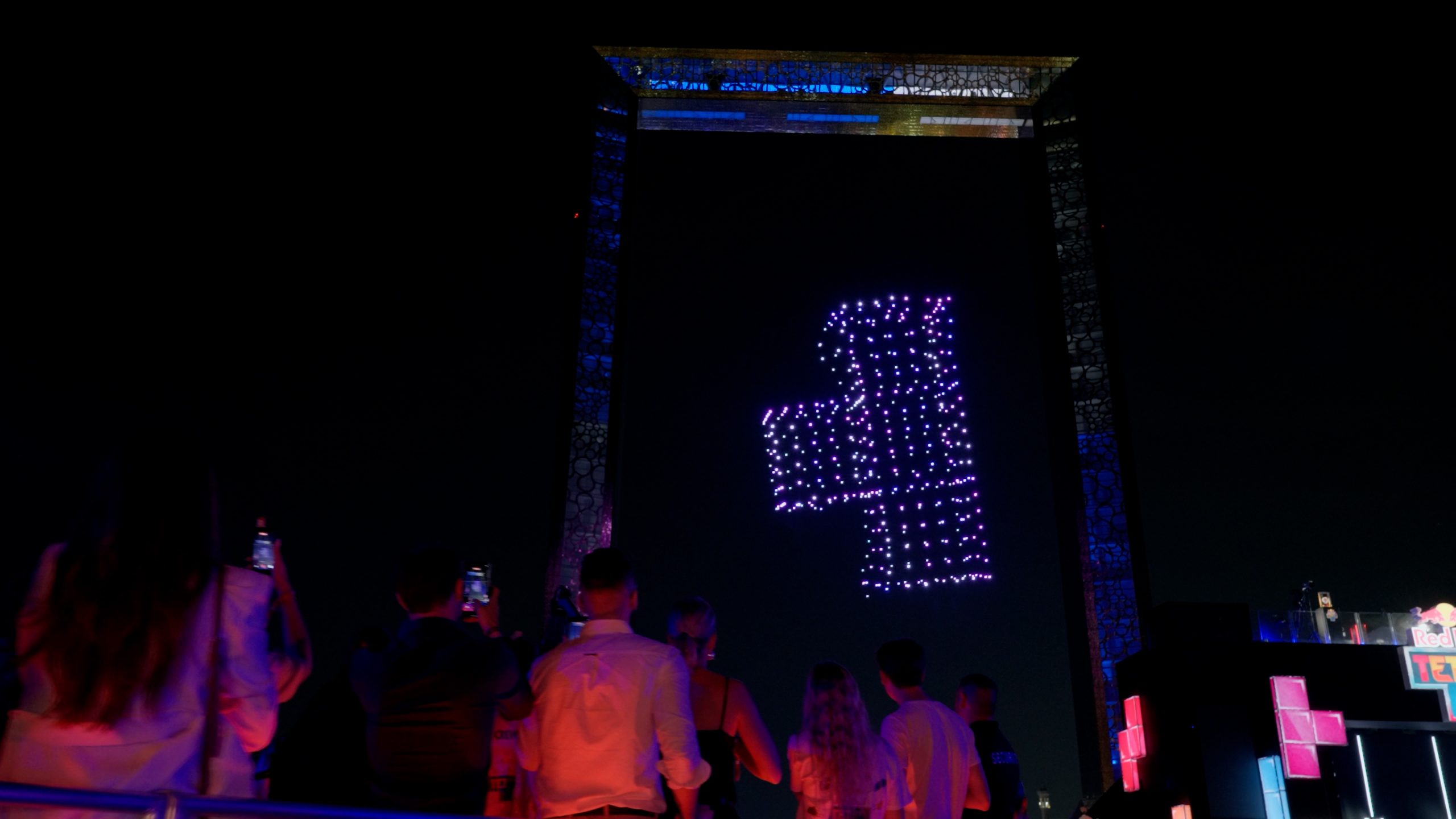 During the Red Bull Tetris Final in Dubai, the skyscraper's facade displays a massive glowing Tetris figure created by Lumasky's 4,000 Drone Show, with spectators watching from below.